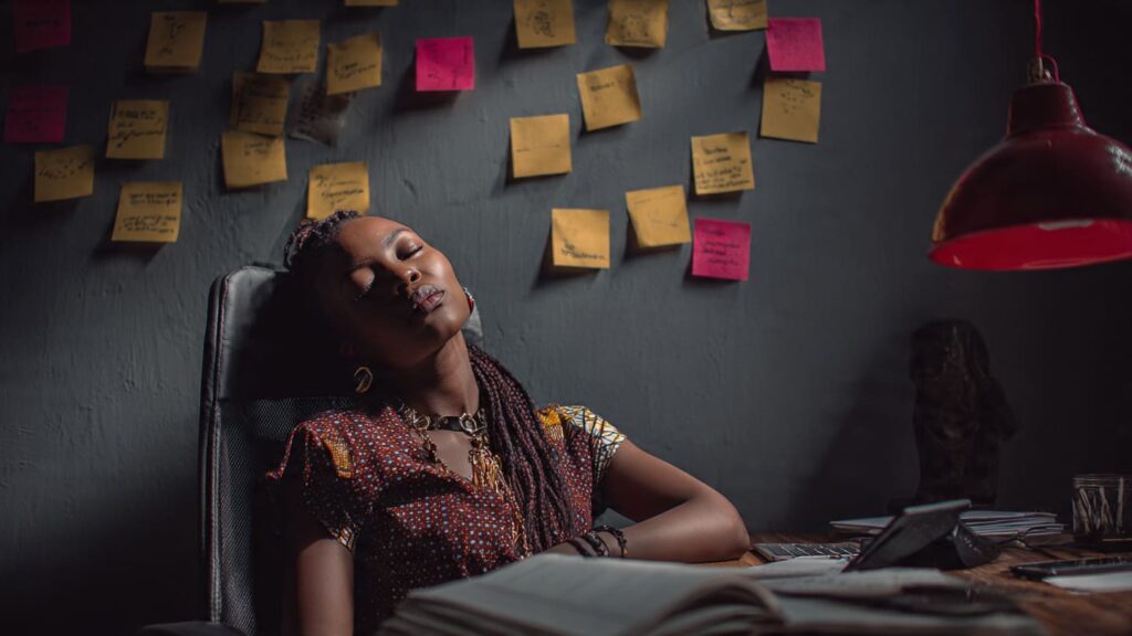 Nigerian female creator surrounded by Post-it notes trend lists and devices looking burned out from random content creation